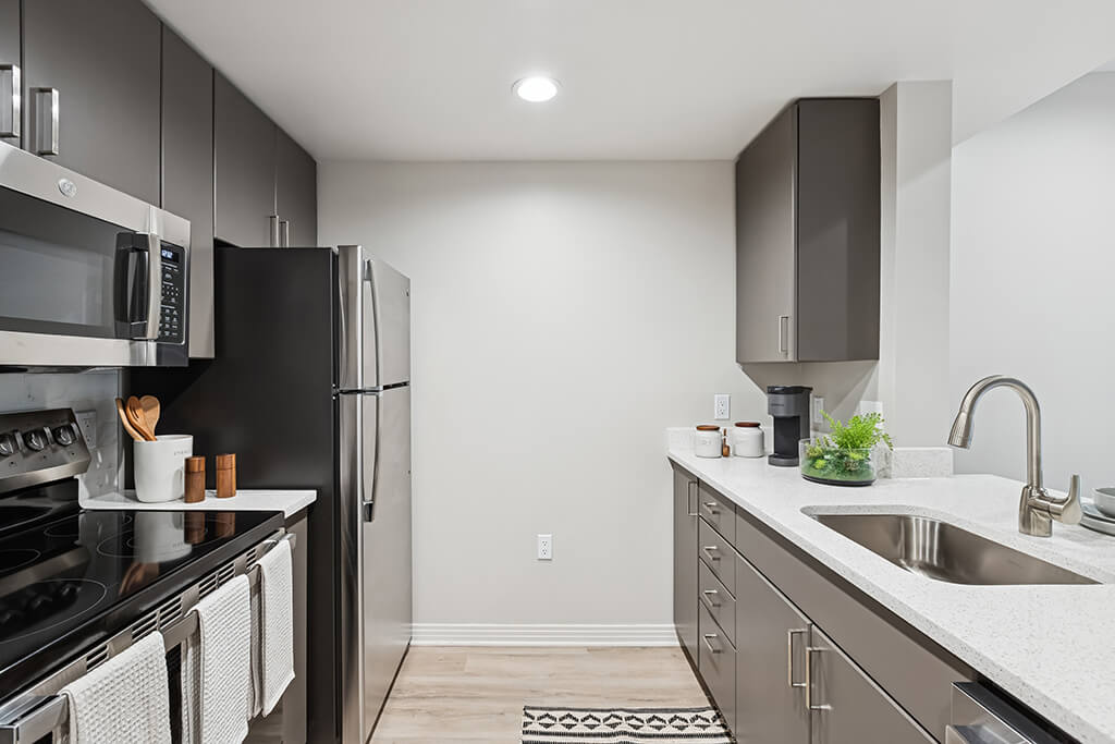 A kitchen with white appliances and wooden cabinets at the Haven at Del Mar Station Apartments in Los Angeles, California.